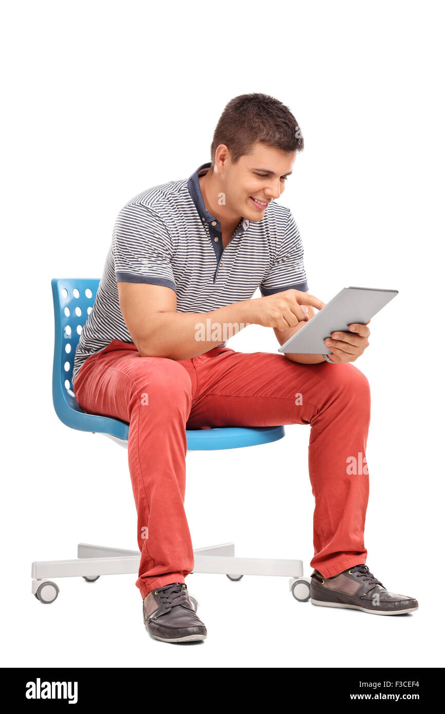 Shot vertical d'un jeune homme assis sur une chaise et travaillant sur un comprimé isolé sur fond blanc Banque D'Images Shot vertical d'un jeune homme assis sur une chaise et travaillant sur un comprimé isolé sur fond blanc Banque D'Images