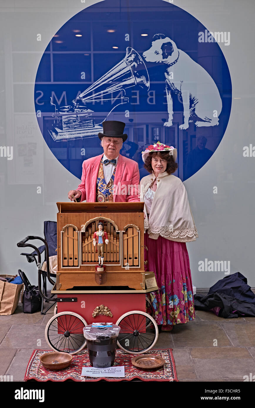 Meuleuse d'organes Royaume-Uni.Meuleuses d'orgue pour époux et épouse vêtues d'une robe traditionnelle vintage contre l'emblématique insigne HMV.Street Entertainers Angleterre Banque D'Images
