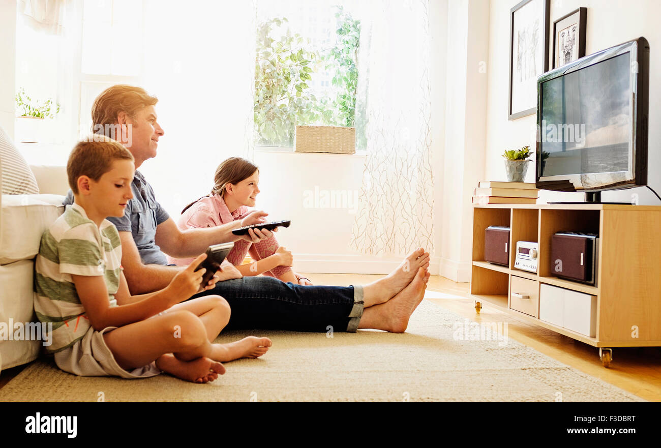 Enfants (8-9, 10-11) regarder la TV avec leur père Banque D'Images