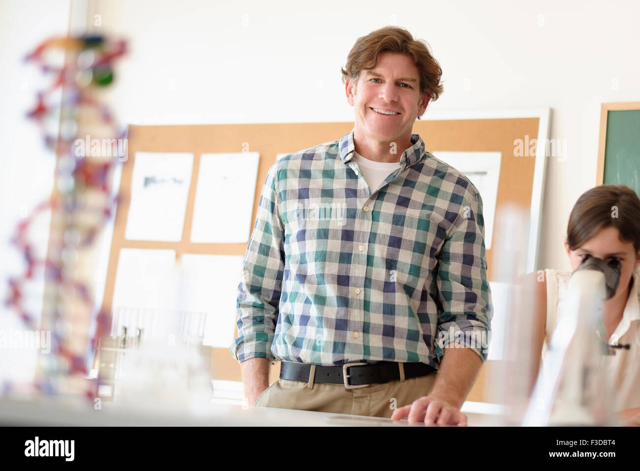 Portrait d'enseignant à l'intérieur, girl (10-11) using microscope in background Banque D'Images