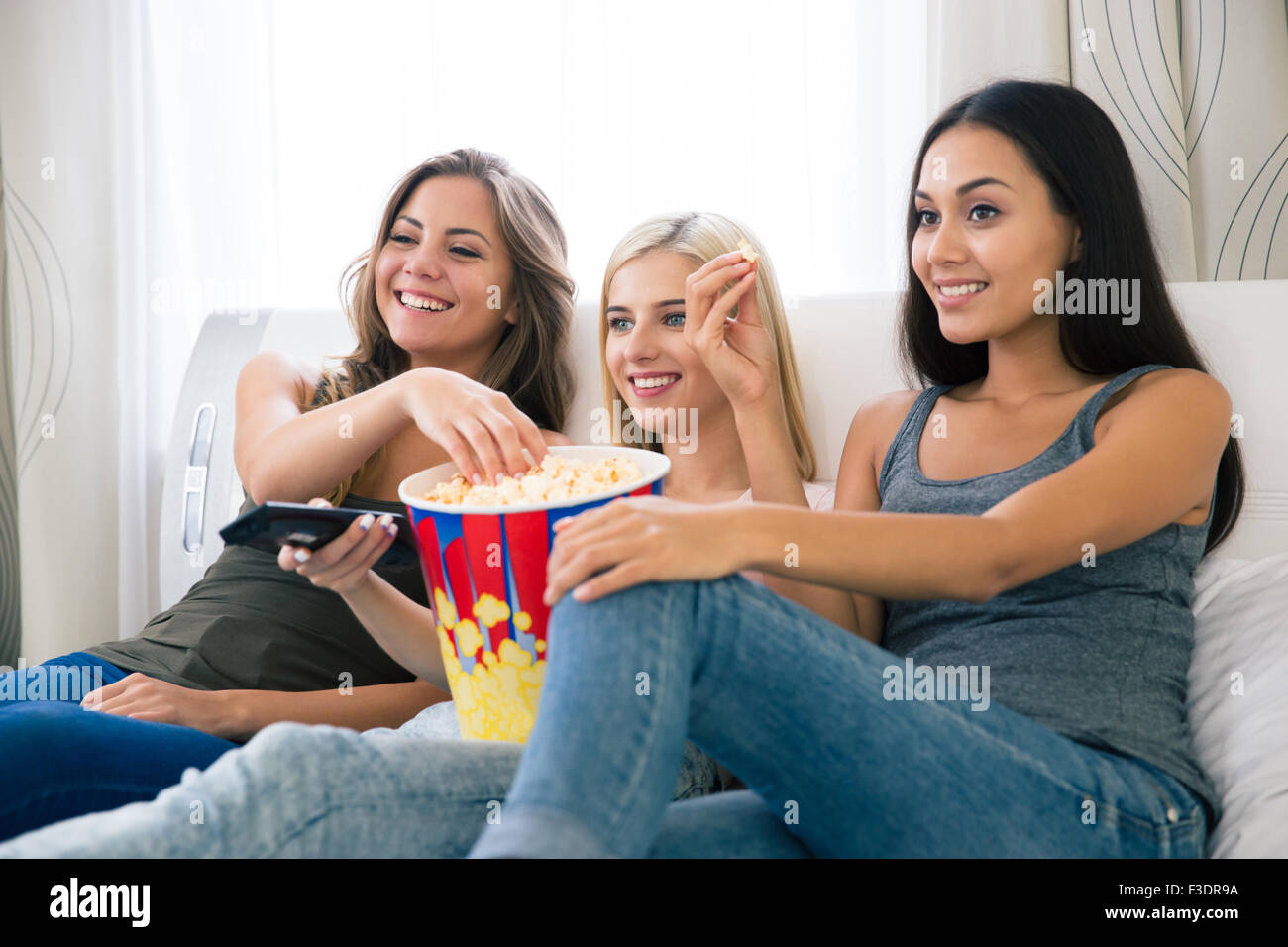Portrait de trois professionnels girlfriends eating popcorn et regarder la télé à la maison Banque D'Images