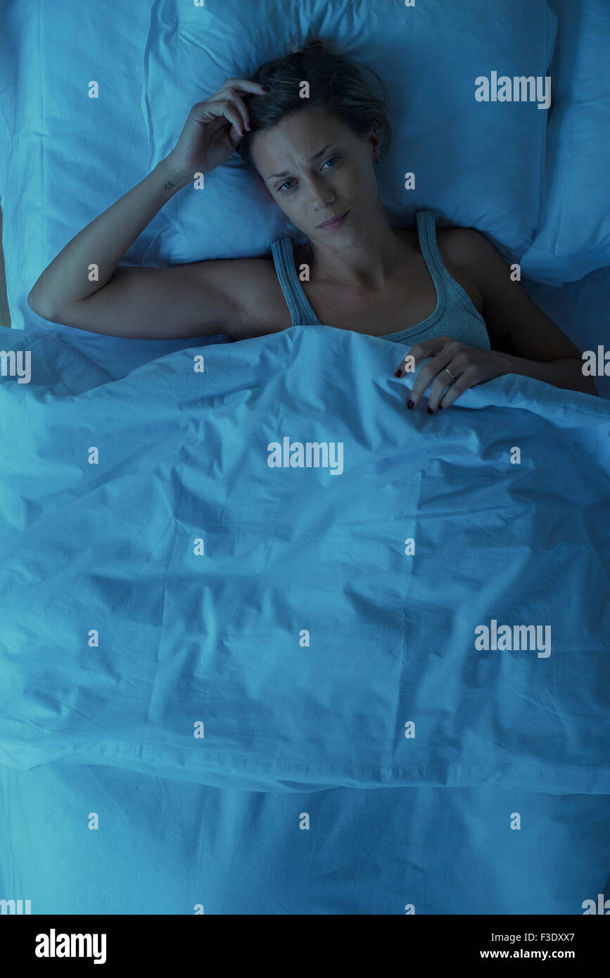 Woman lying awake au lit avec l'expression inquiète sur le visage Banque D'Images