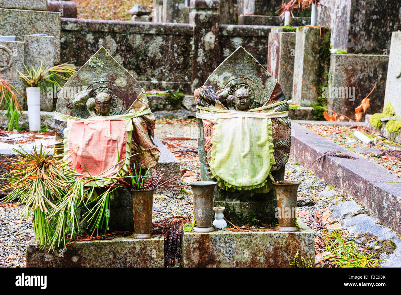 Le Japon, Koyasan, Okunoin cemetery. Deux statues jizo bosatsu bibbed placé sur les pierres tombales, côte à côte. Pierres tombales leur tête. Banque D'Images