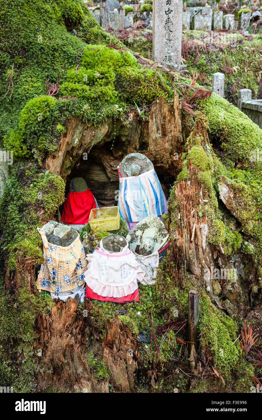 Le Japon, Koyasan, cimetière Okunoin. Groupe de cinq statues en pierre jizo bosatsu bibbed et plastique panier collection en cèdre évidé tronc d'arbre. Banque D'Images
