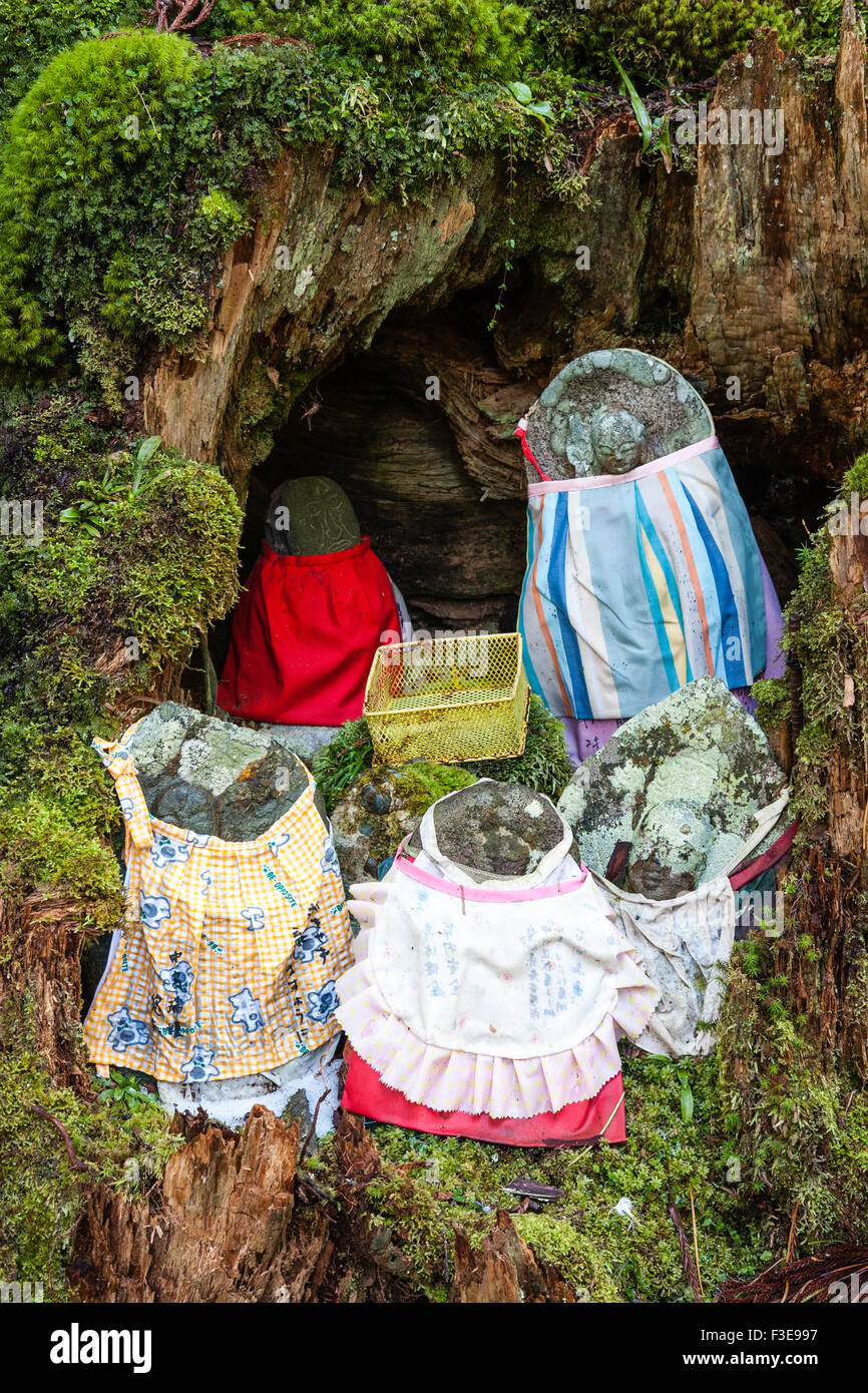 Le Japon, Koyasan, cimetière Okunoin. Groupe de cinq statues en pierre jizo bosatsu bibbed et plastique panier collection en cèdre évidé tronc d'arbre. Banque D'Images