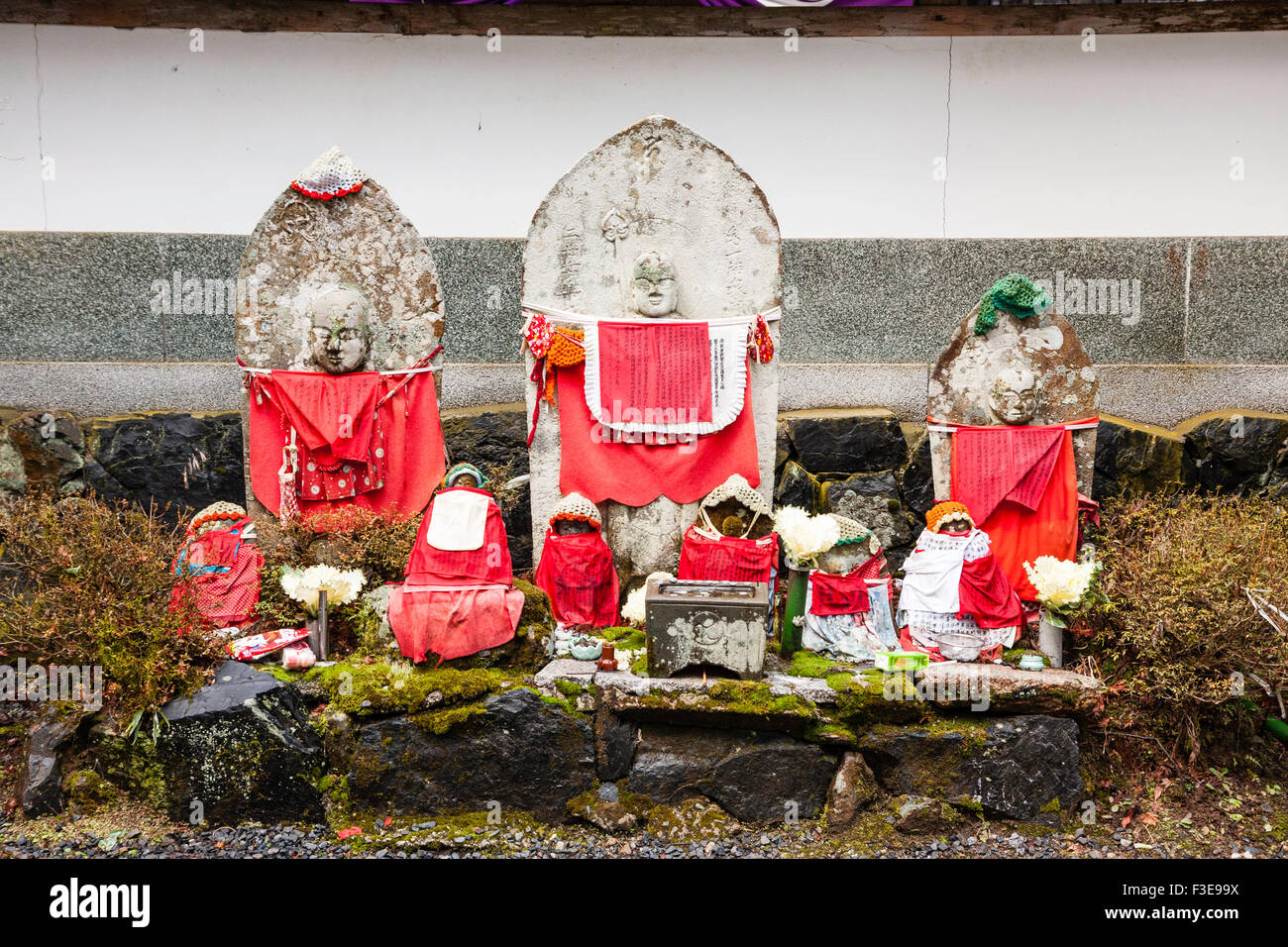 Le Japon, Koyasan, cimetière Okunoin. Groupe de statues jizo bibbed rouge, 3 grandes à l'arrière et plusieurs petits en face de pierre placé sur l'étape. Banque D'Images