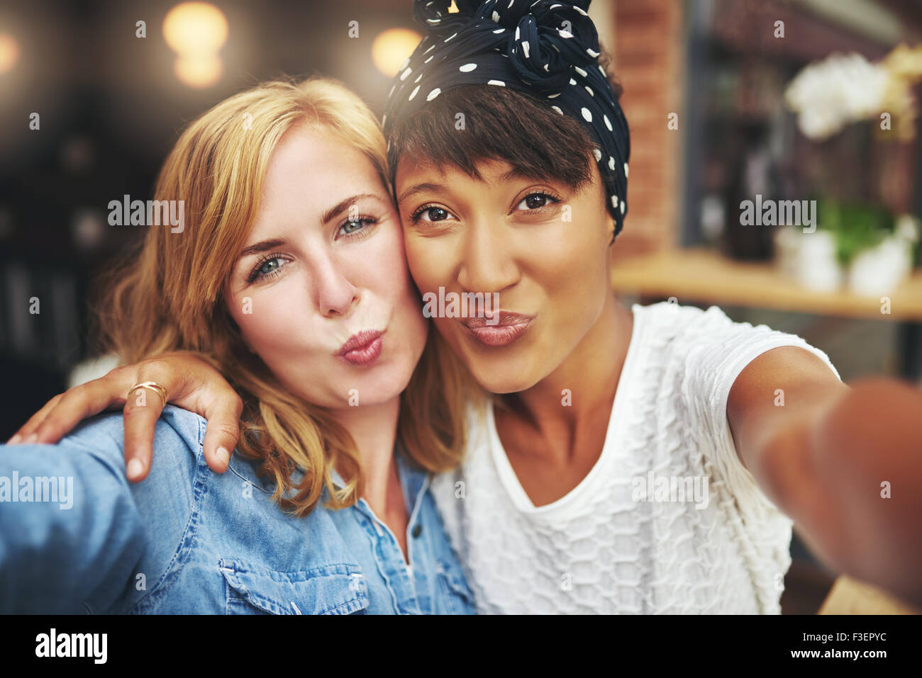 Deux jeunes femmes ludique attrayant debout dans les bras, poussant un baiser à la caméra de froisser leurs lèvres avec un sourire taquinant Banque D'Images