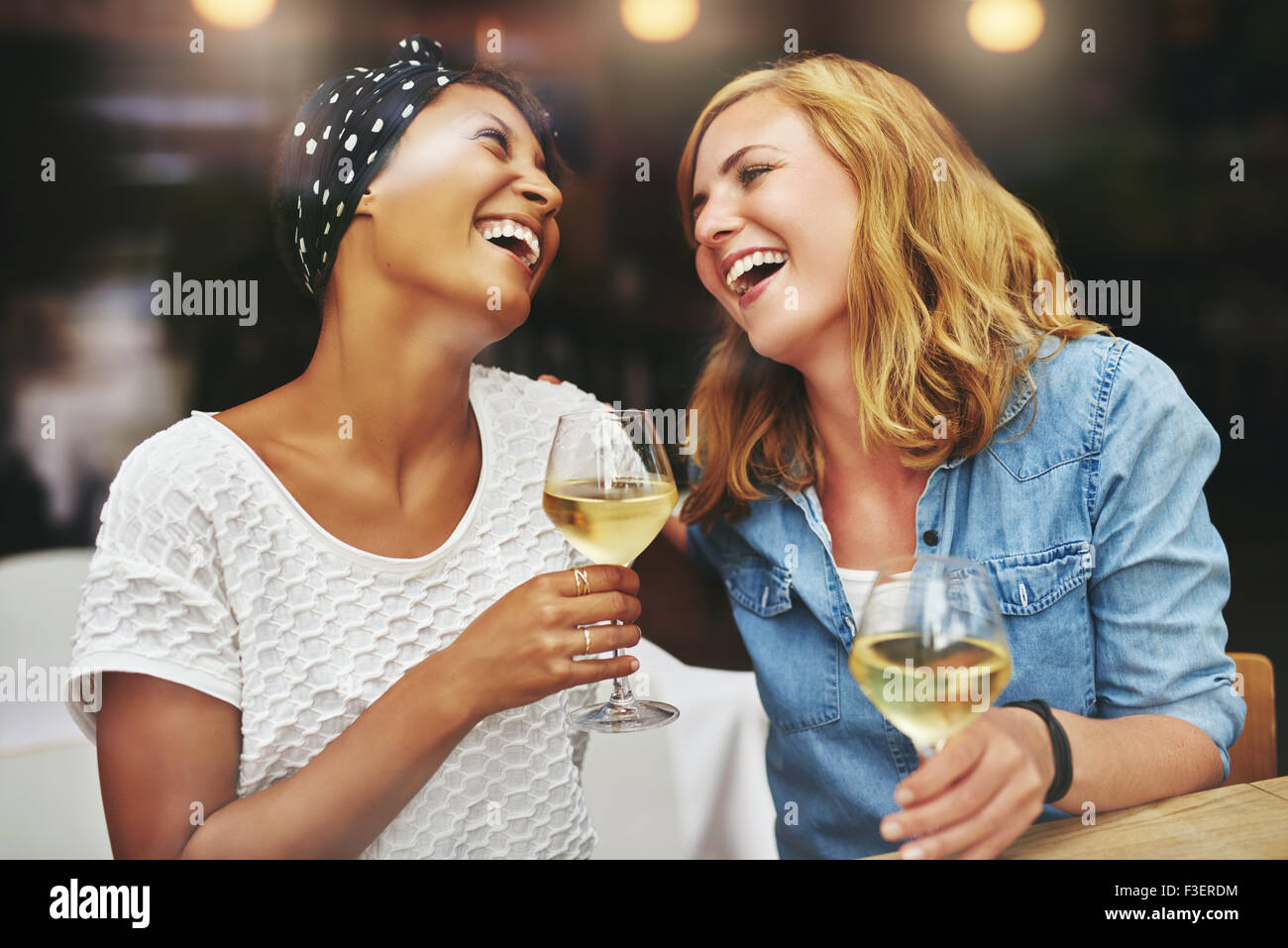 Deux jeunes femmes multiethniques de vivacité attrayant friends et rire ensemble autour d'un verre de vin blanc Banque D'Images