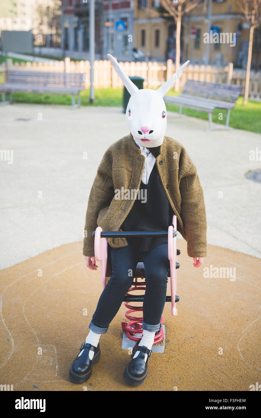 Belle jeune femme asiatique hipster assis sur un jouet dans un terrain de jeux portant un masque de lapin - carnaval, halloween, concept fou Banque D'Images