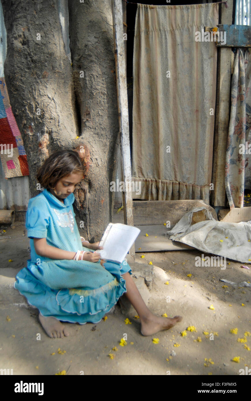 Une fille de l'ouvrier routier apprend Marathi alphabets sous un arbre ; Bombay maintenant Mumbai Maharashtra ; Inde ; Banque D'Images