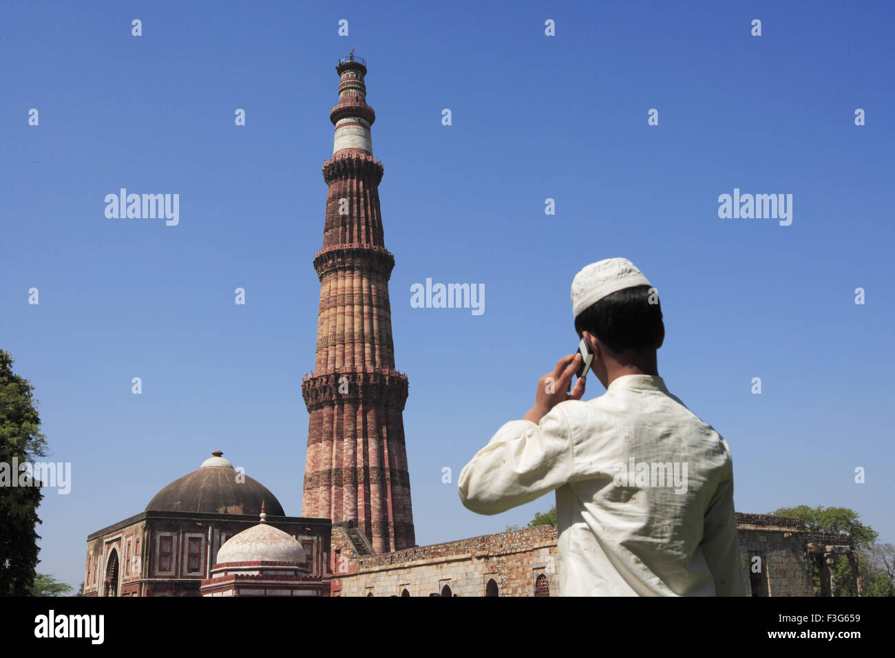 Garçon musulman talking on mobile phone at Qutab Minar construit en 1311 en grès rouge l'art musulman Indo tour Delhi Banque D'Images