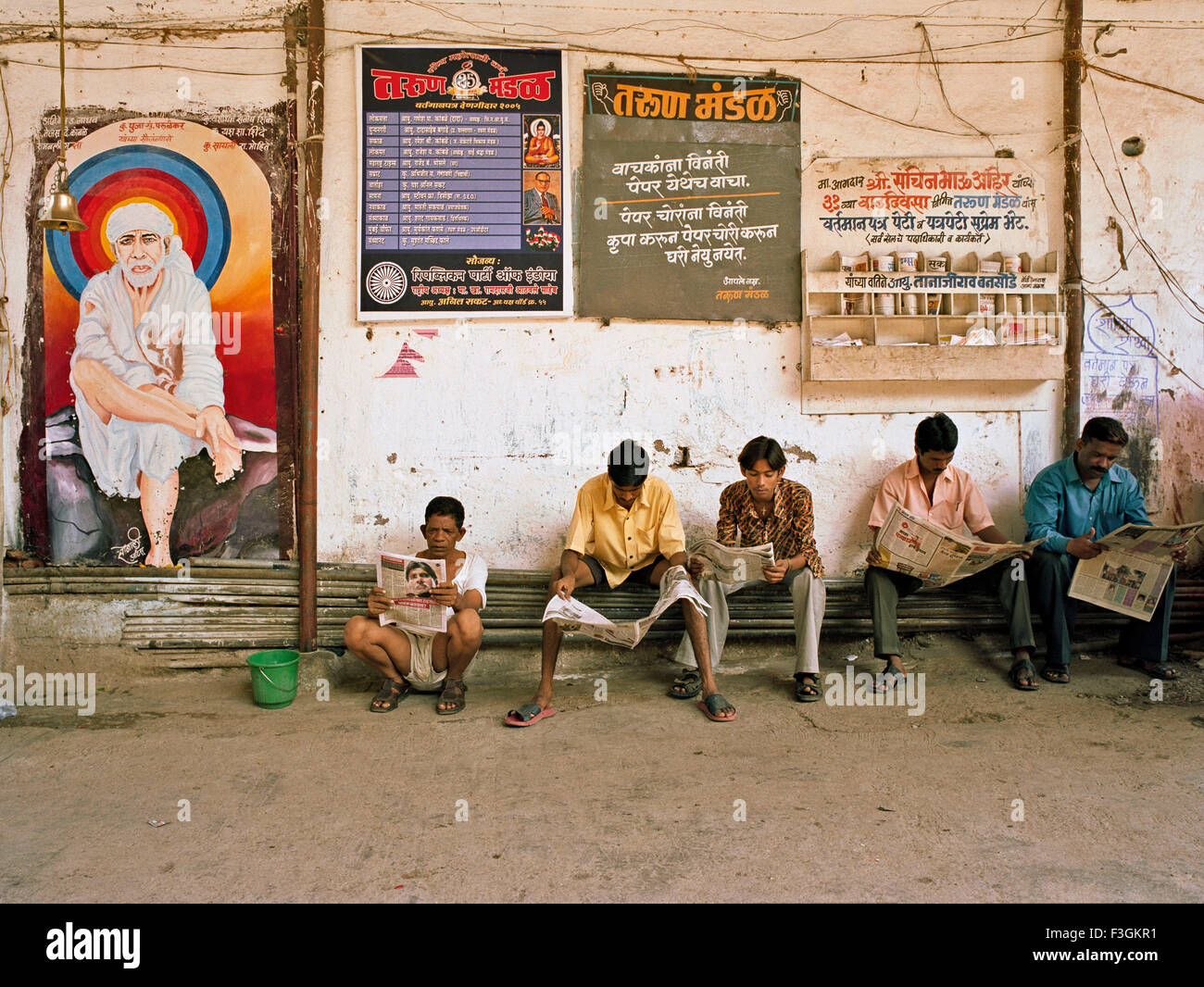 Les gens qui lisent les quotidiens assis sur des tuyaux d'eau ; Bombay ; Mumbai ; Maharashtra ; Inde ; Asie Banque D'Images