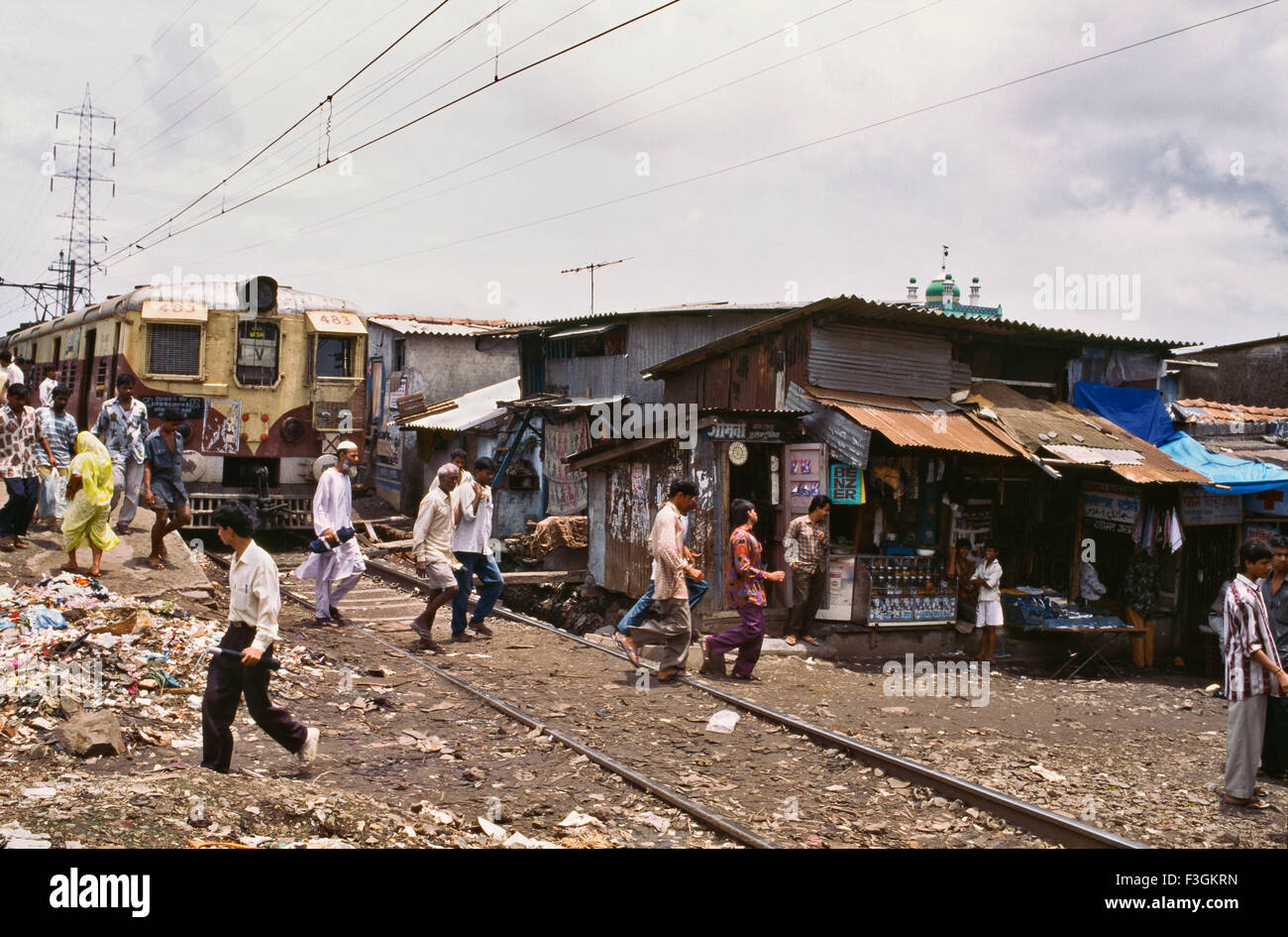 Passage à niveau ligne de chemin de fer de banlieue suburban train passe stretch dense avec des bidonvilles le long de son côté à Govandi gare Mumbai Banque D'Images