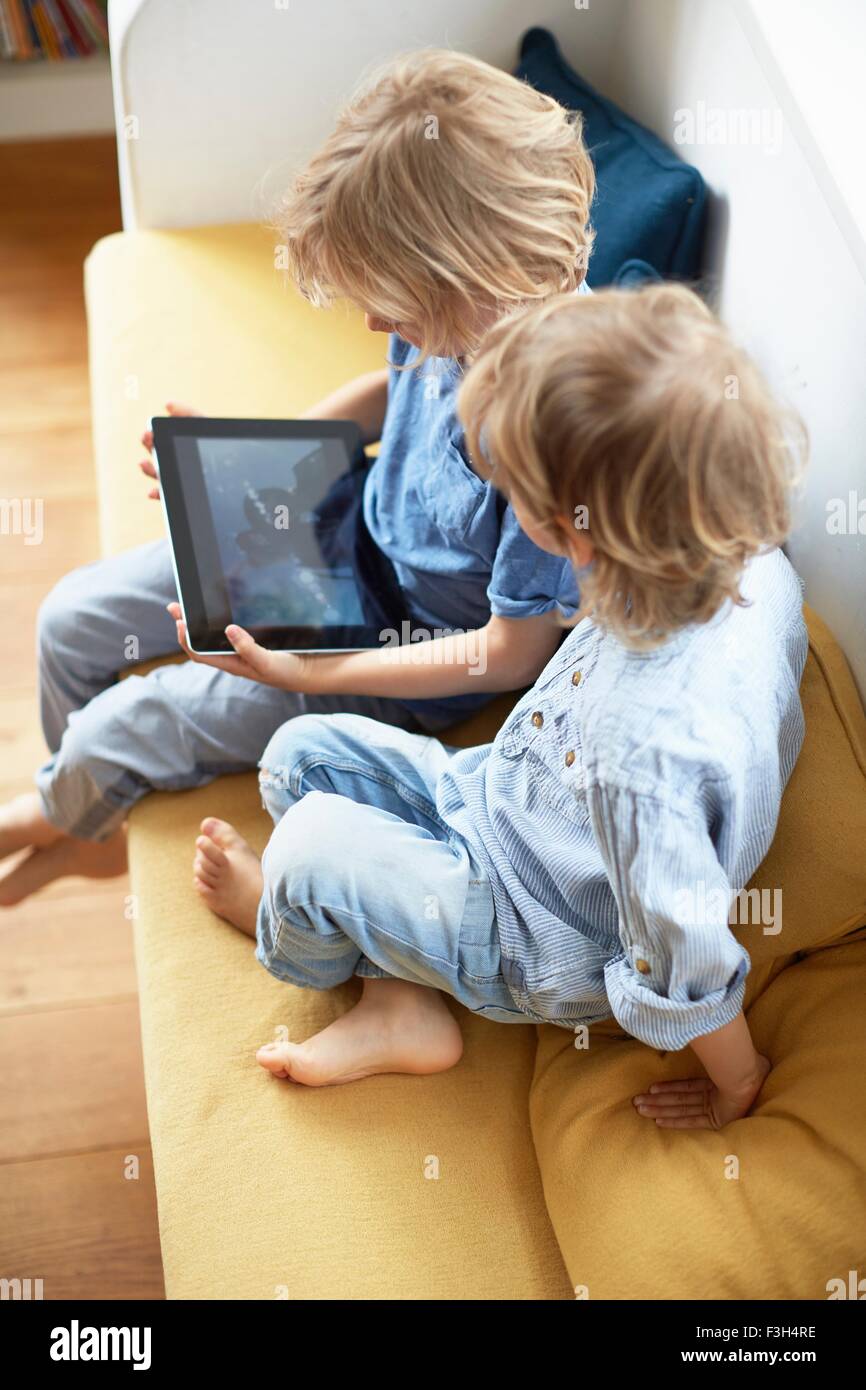 Deux jeunes garçons, assis sur le canapé, looking at digital tablet Banque D'Images
