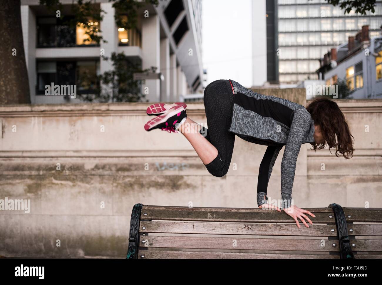 Jeune femme sautant au-dessus de banc de parc en ville Banque D'Images