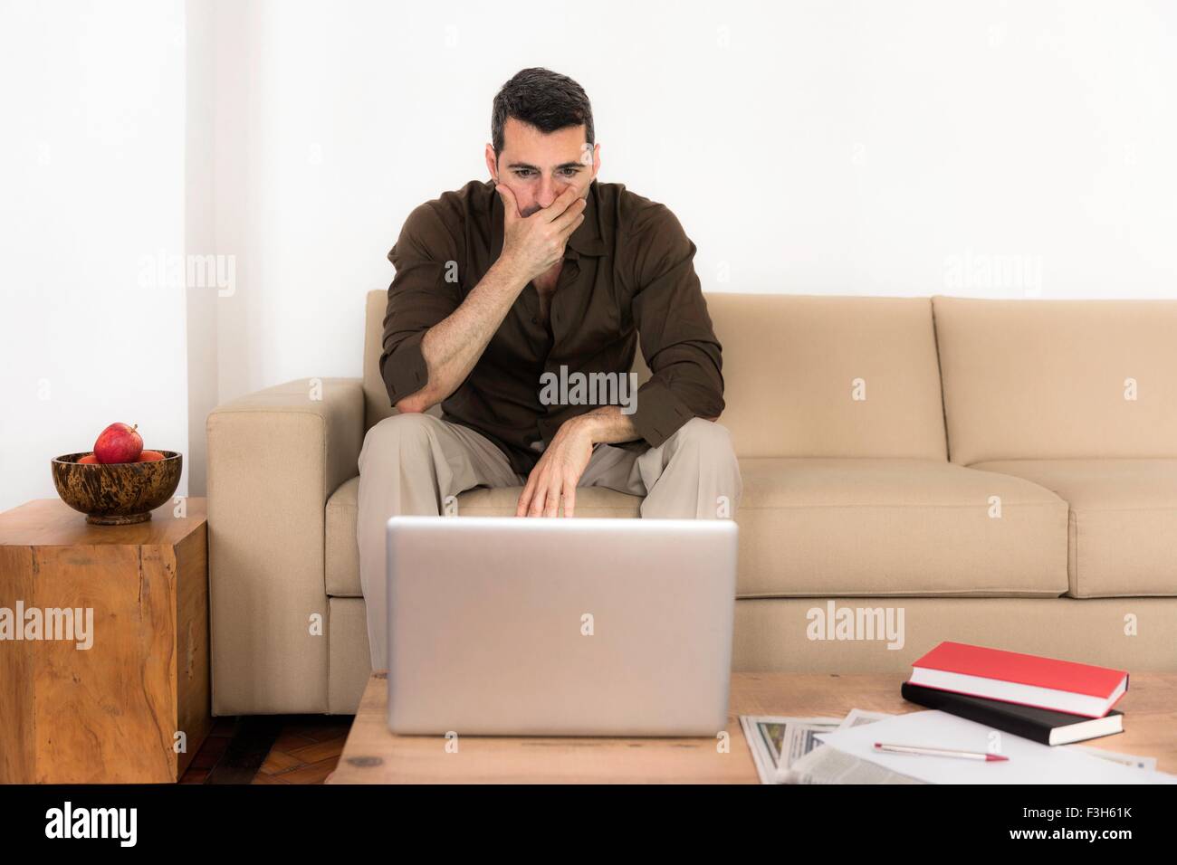 Young man looking at laptop, main sur la bouche Banque D'Images