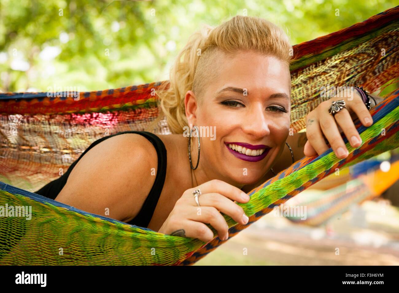 Portrait of mid adult woman with shaved cheveux blonds couché dans un hamac de jardin Banque D'Images