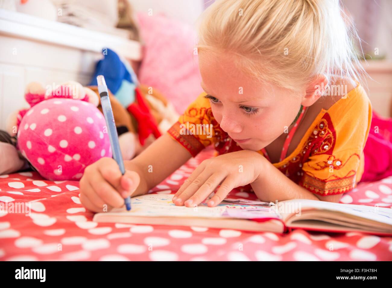 Girl lying on bed jouant le dessin dans un livre à colorier Banque D'Images