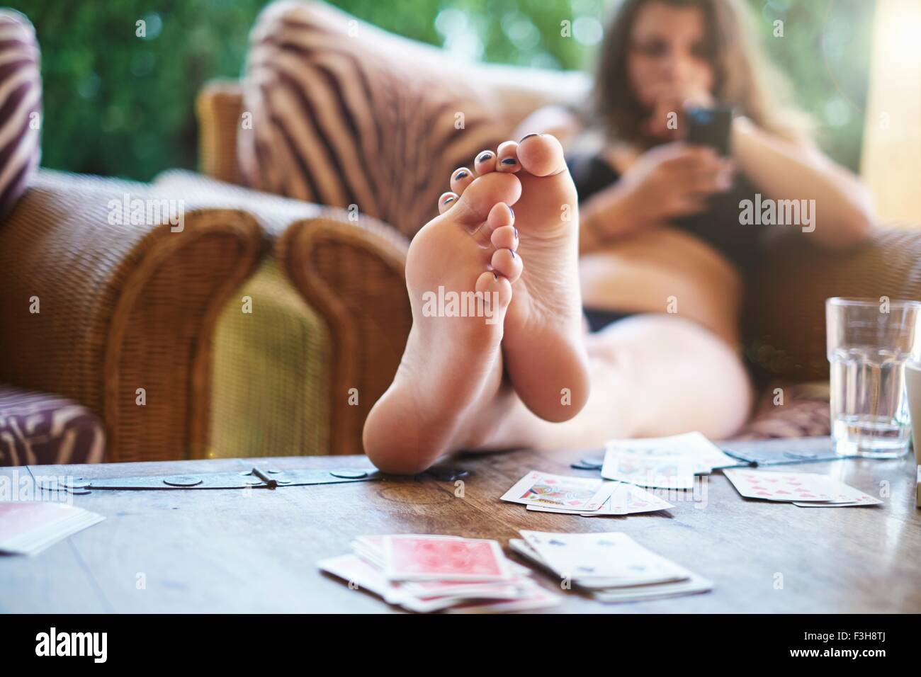Teenage girl reading textes smartphone avec pieds sur table patio Banque D'Images