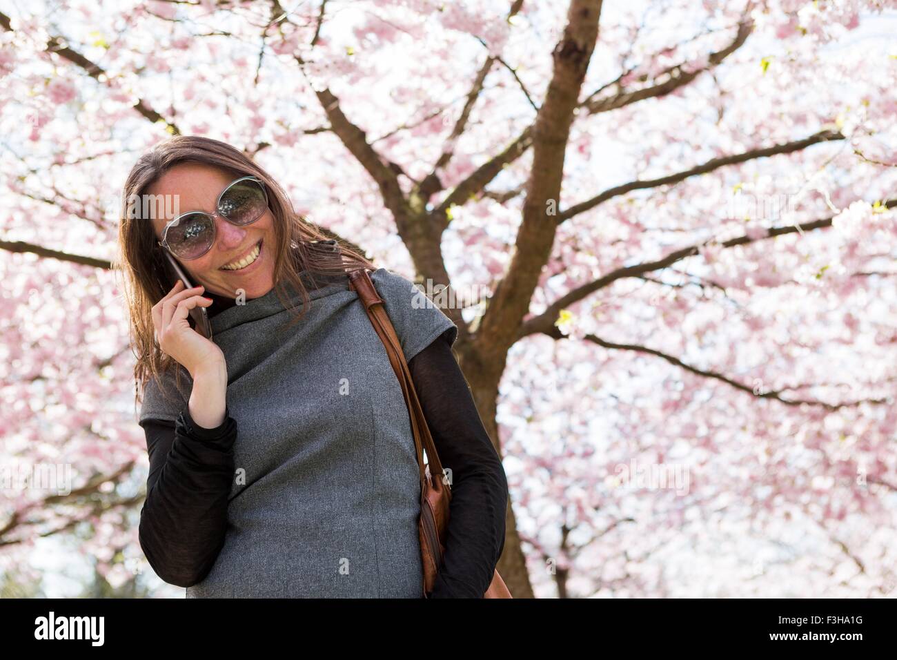 Young woman chatting on smartphone in front of cherry blossom Banque D'Images