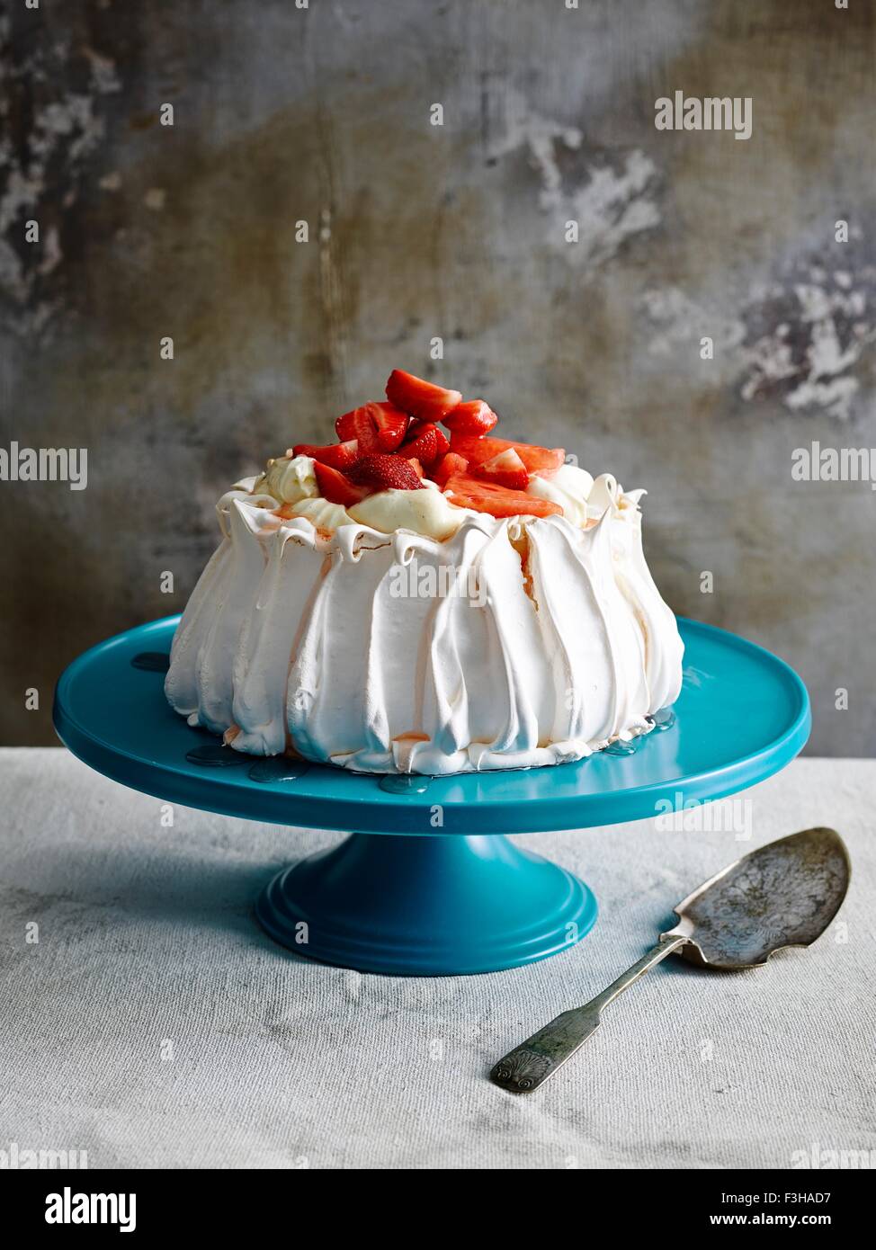 Couverte de fraises pavlova sur céramique bleu cake stand avec cake server Banque D'Images