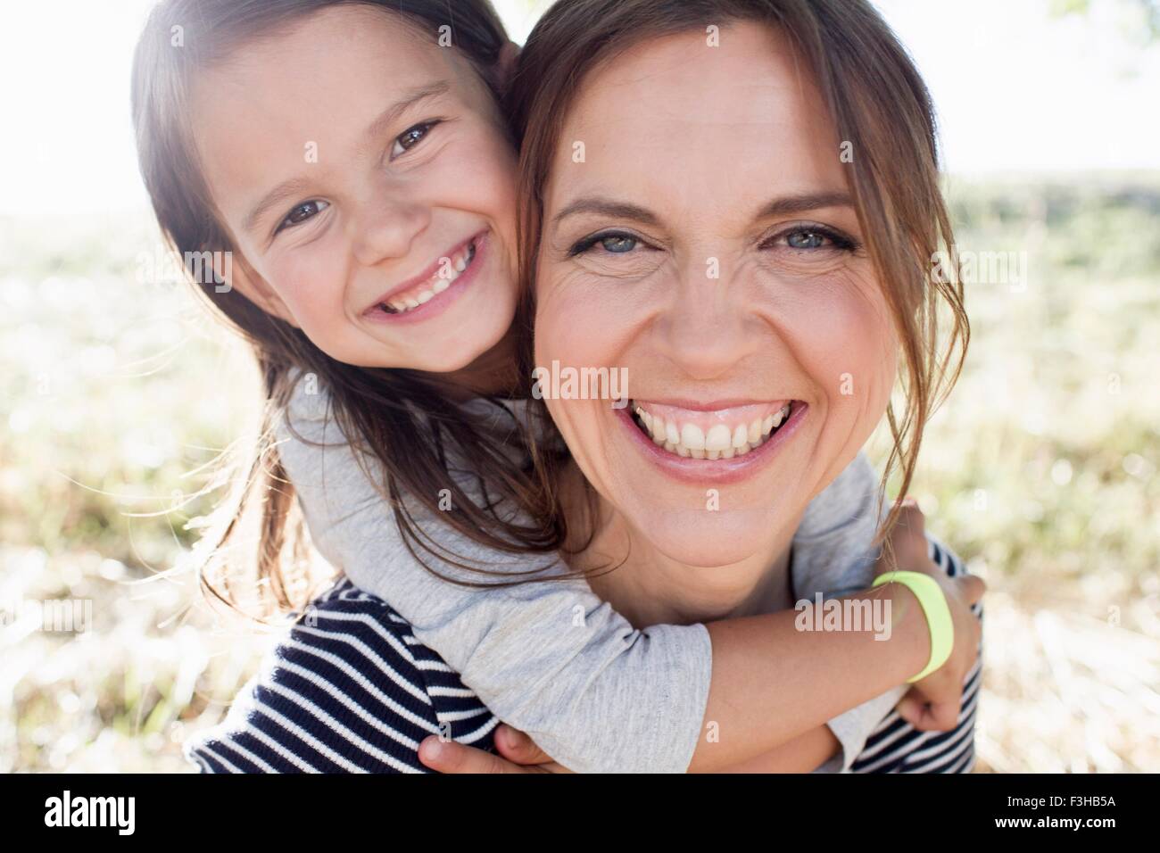 Portrait of young woman giving daughter piggy back in park Banque D'Images