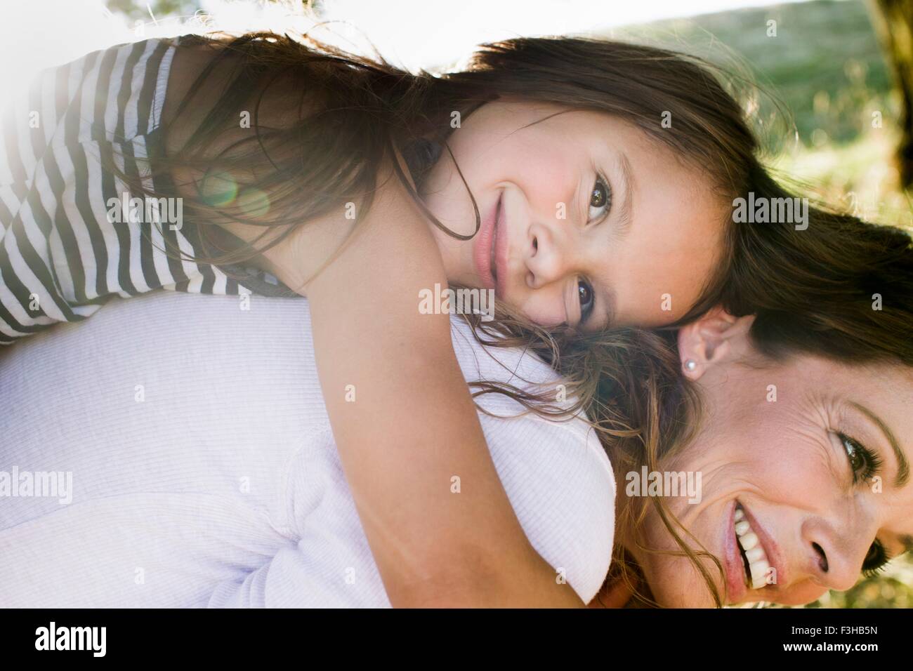 Young woman giving daughter piggy back in park Banque D'Images