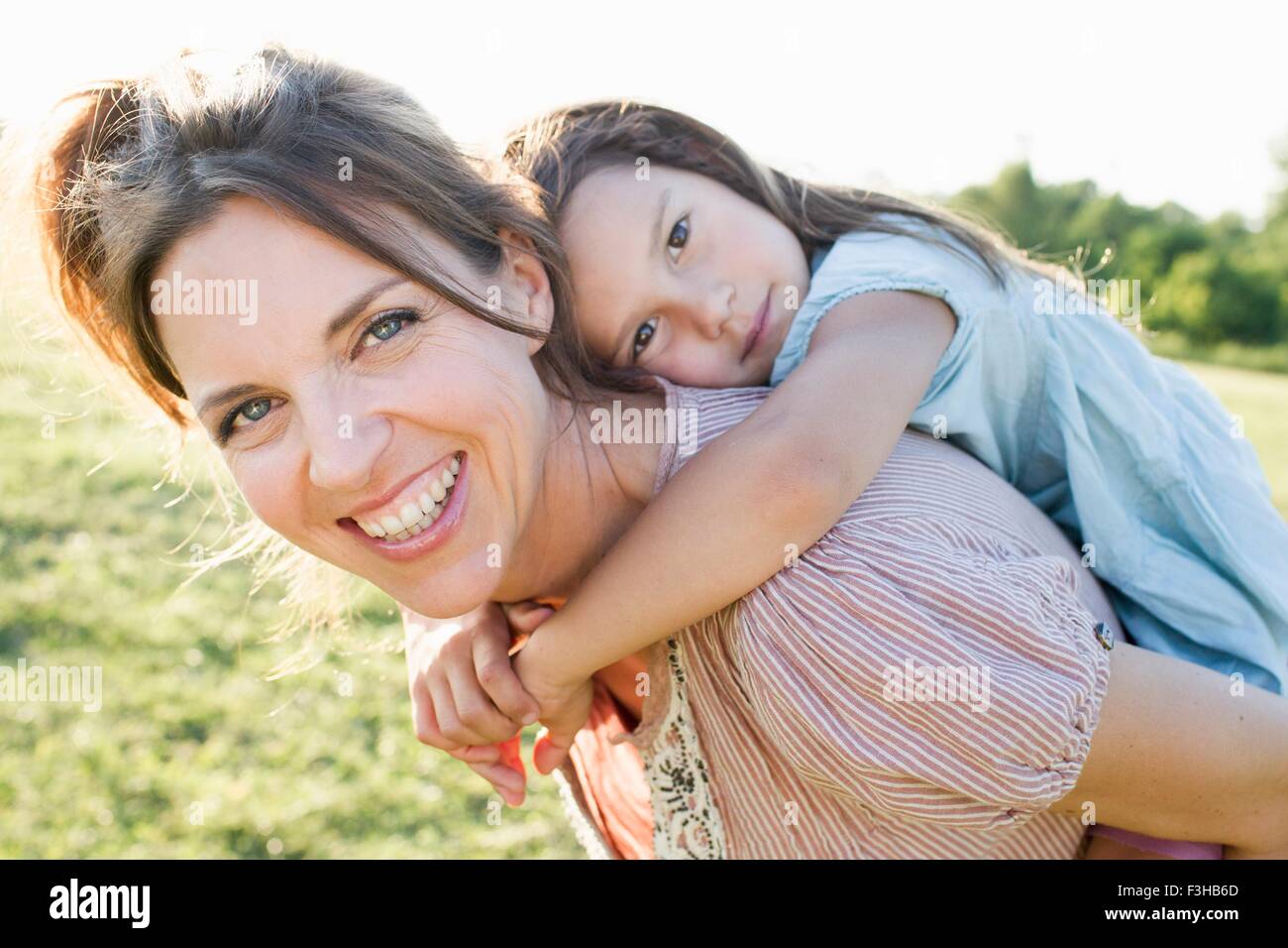 Young woman giving daughter piggy back ride in park Banque D'Images