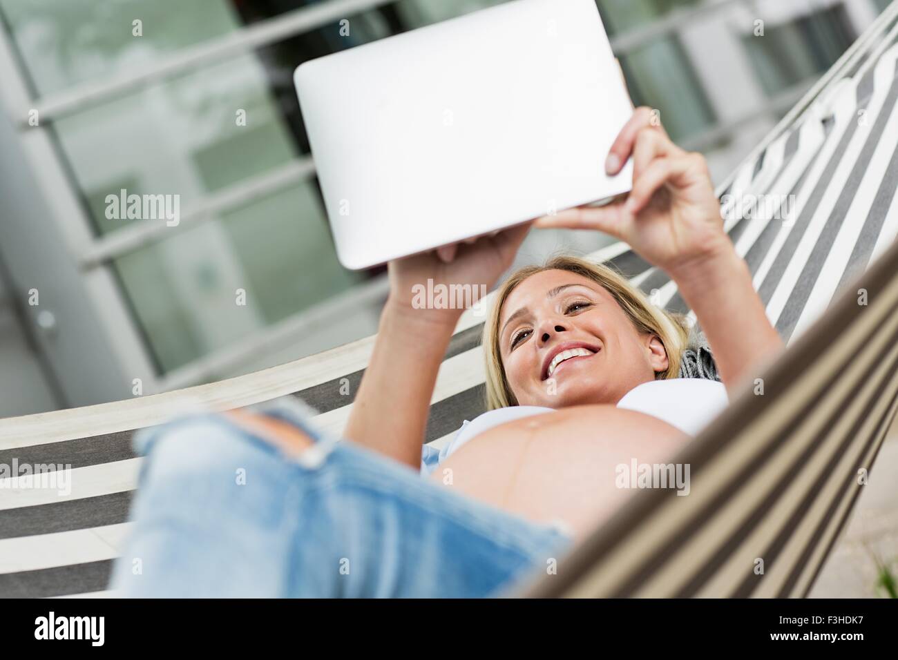 La grossesse à terme young woman lying in hammock using digital tablet Banque D'Images La grossesse à terme young woman lying in hammock using digital tablet Banque D'Images