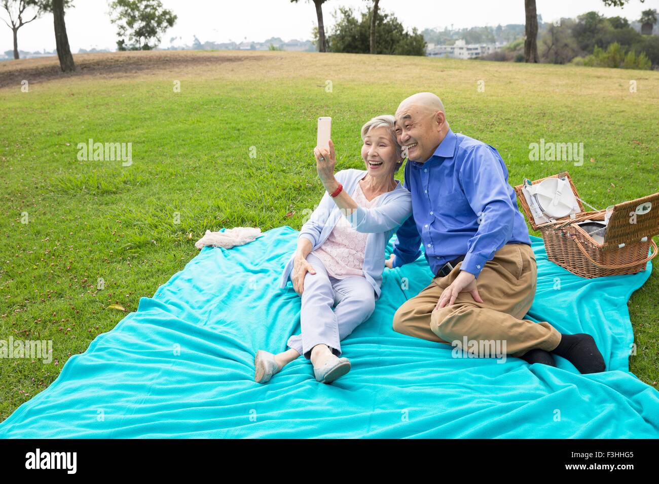 Senior couple having picnic in park, taking self portrait using smartphone Banque D'Images