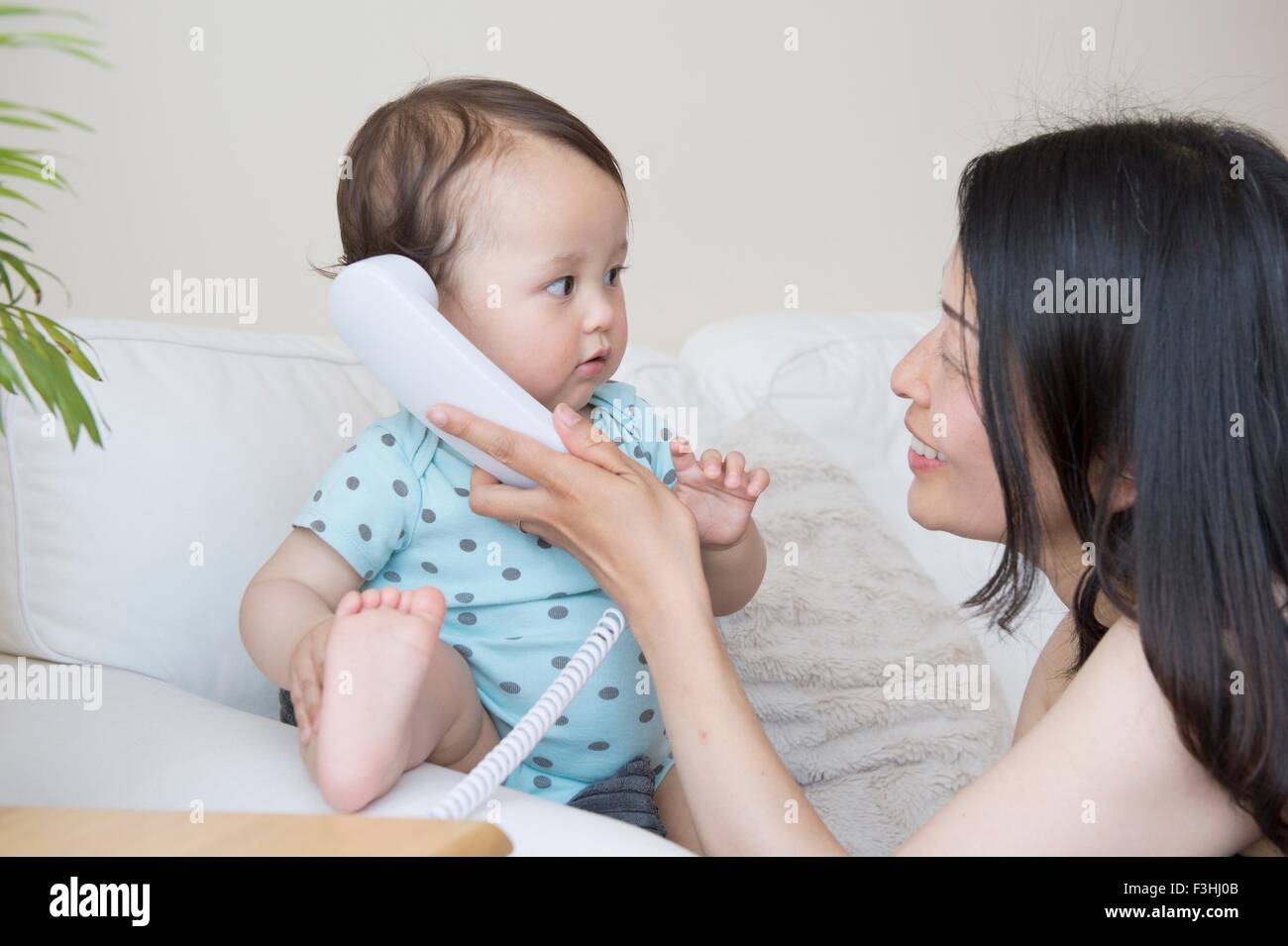 Bébé garçon et la mère à l'écoute de téléphone fixe sur canapé Banque D'Images