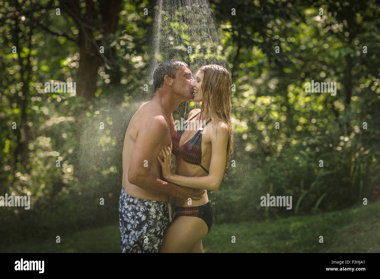Homme mature et jeune amie s'embrasser sous une douche de jardin Banque D'Images