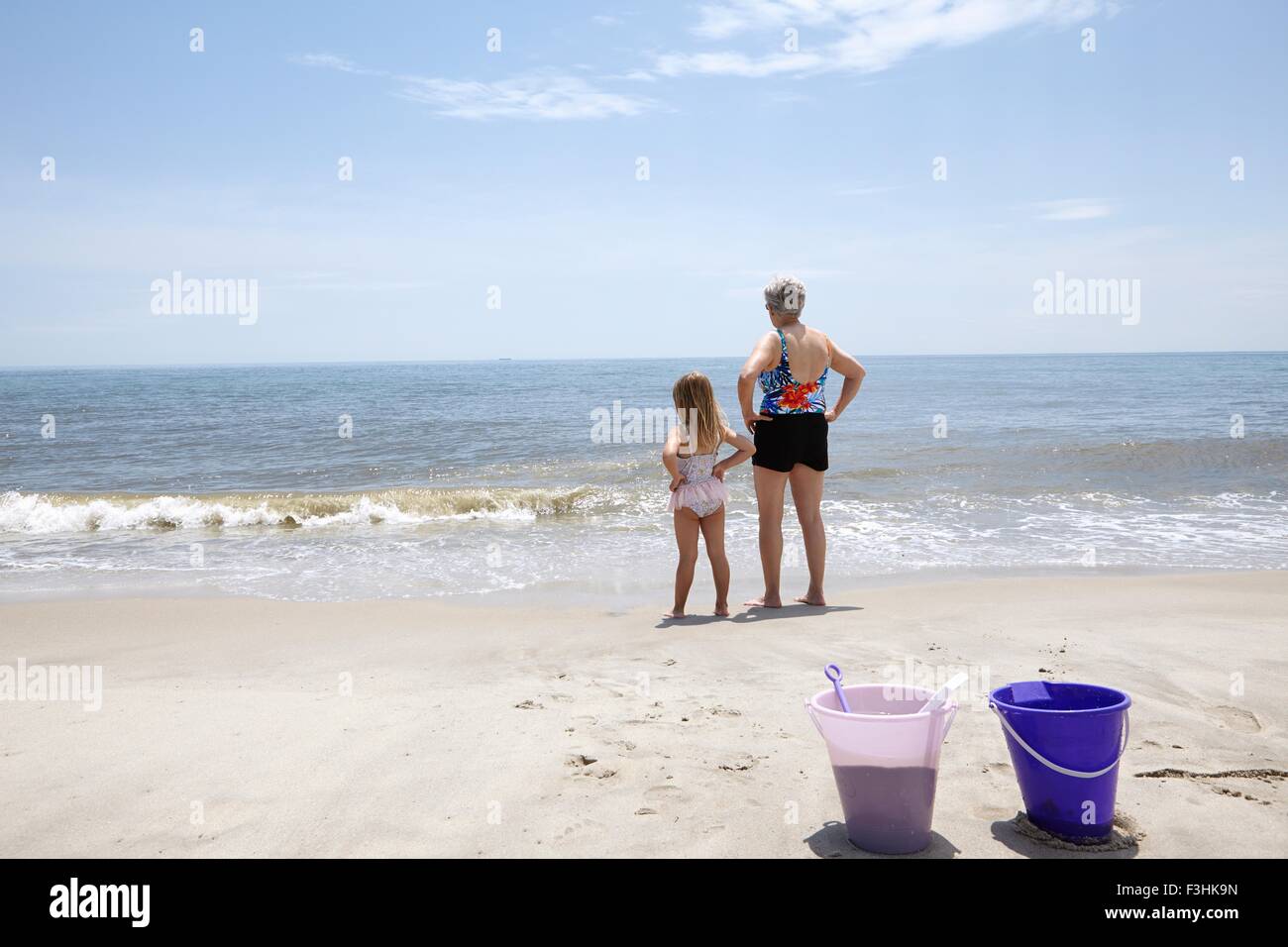 Senior woman avec sa petite-fille avec les mains sur les hanches à la recherche de plage Banque D'Images