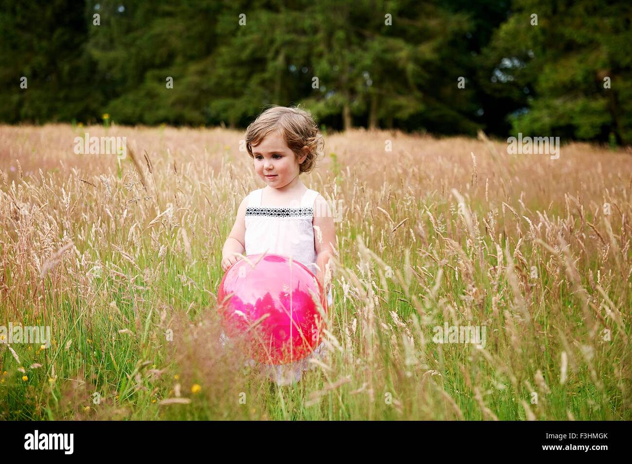 Girl in tall grass holding red balloon looking away Banque D'Images