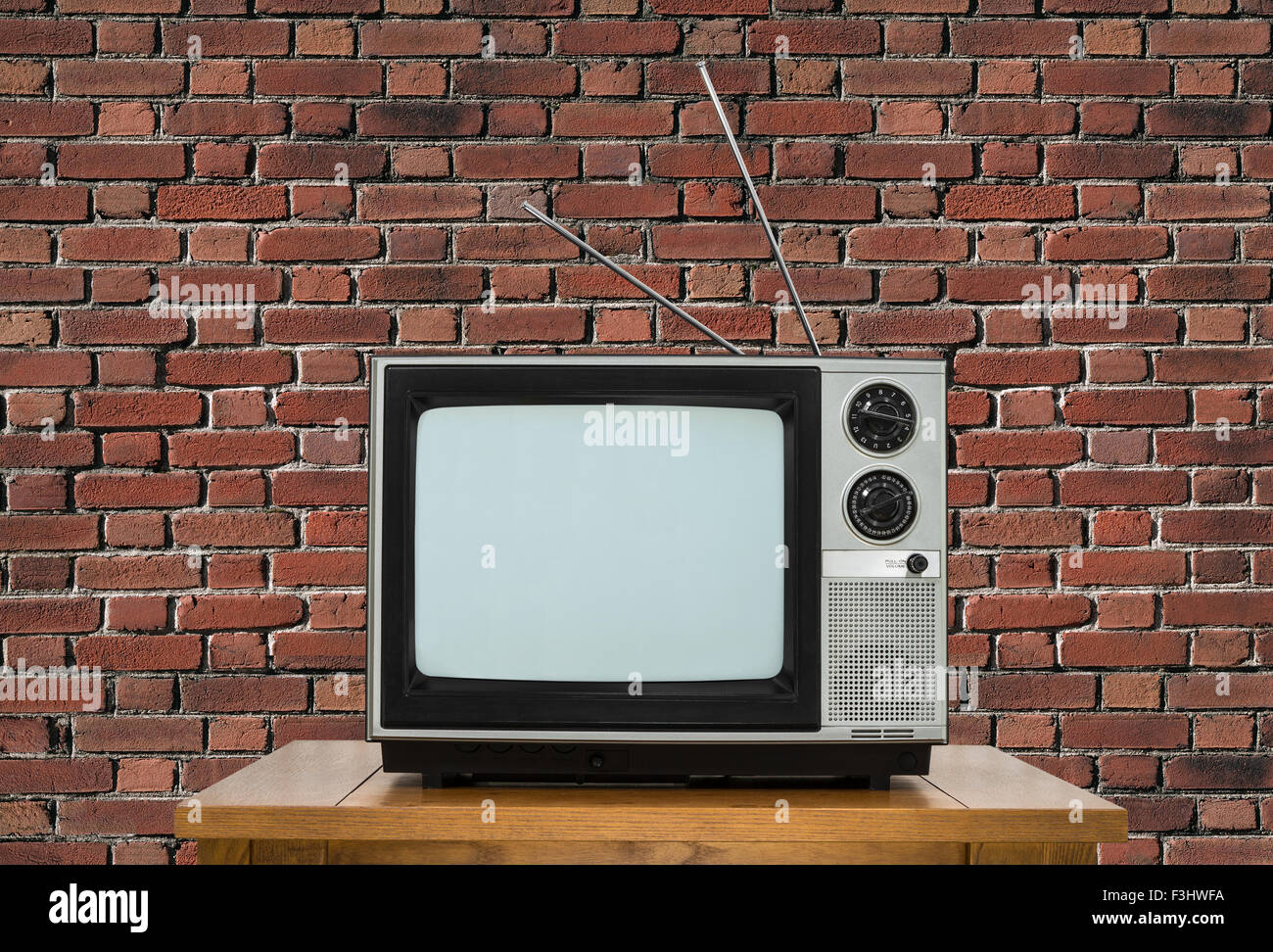 Ancien téléviseur analogique sur table en bois avec mur de brique. Banque D'Images