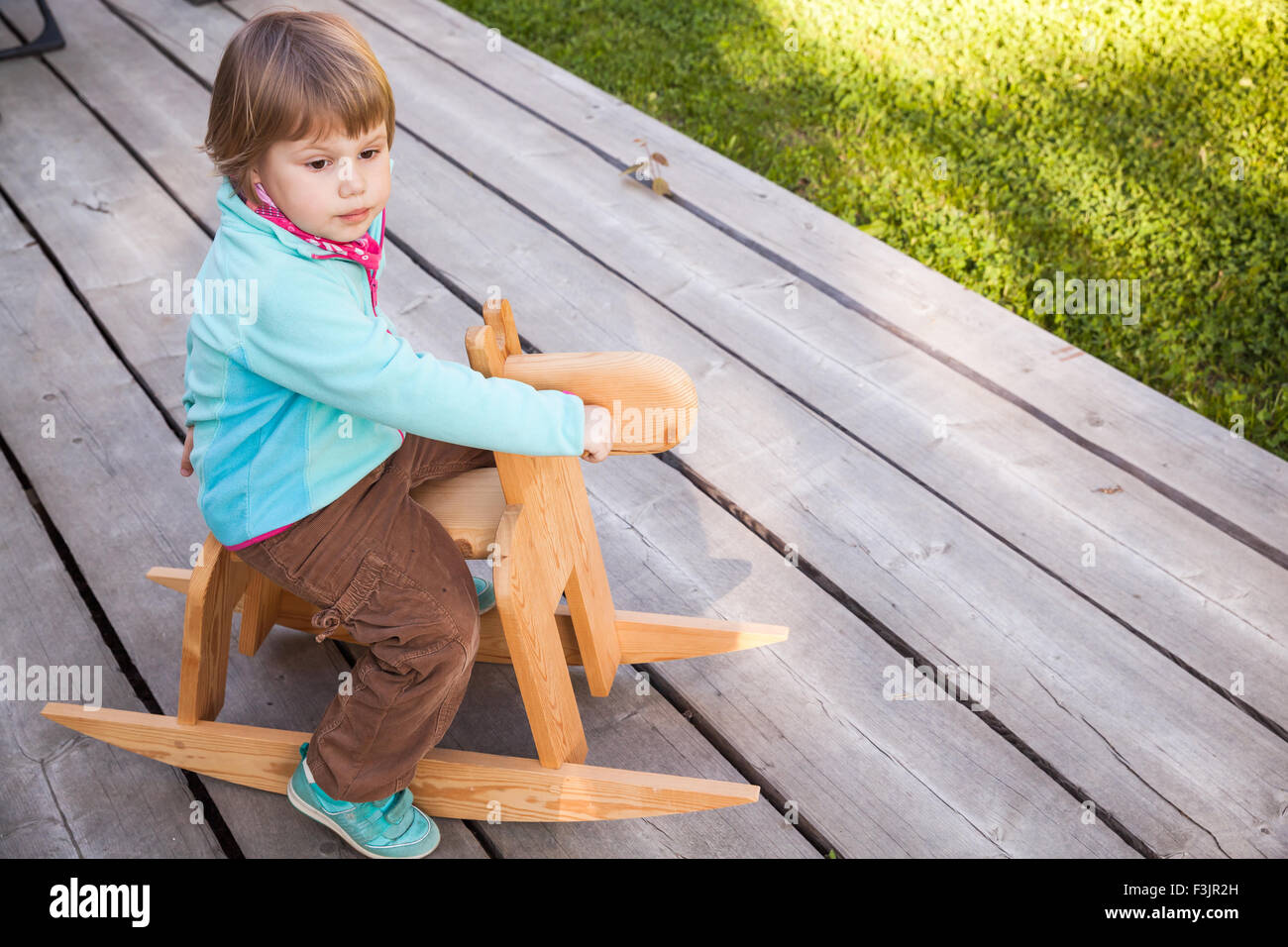 Outdoor portrait of cute young girl riding blond bébé jouet cheval de bois Banque D'Images