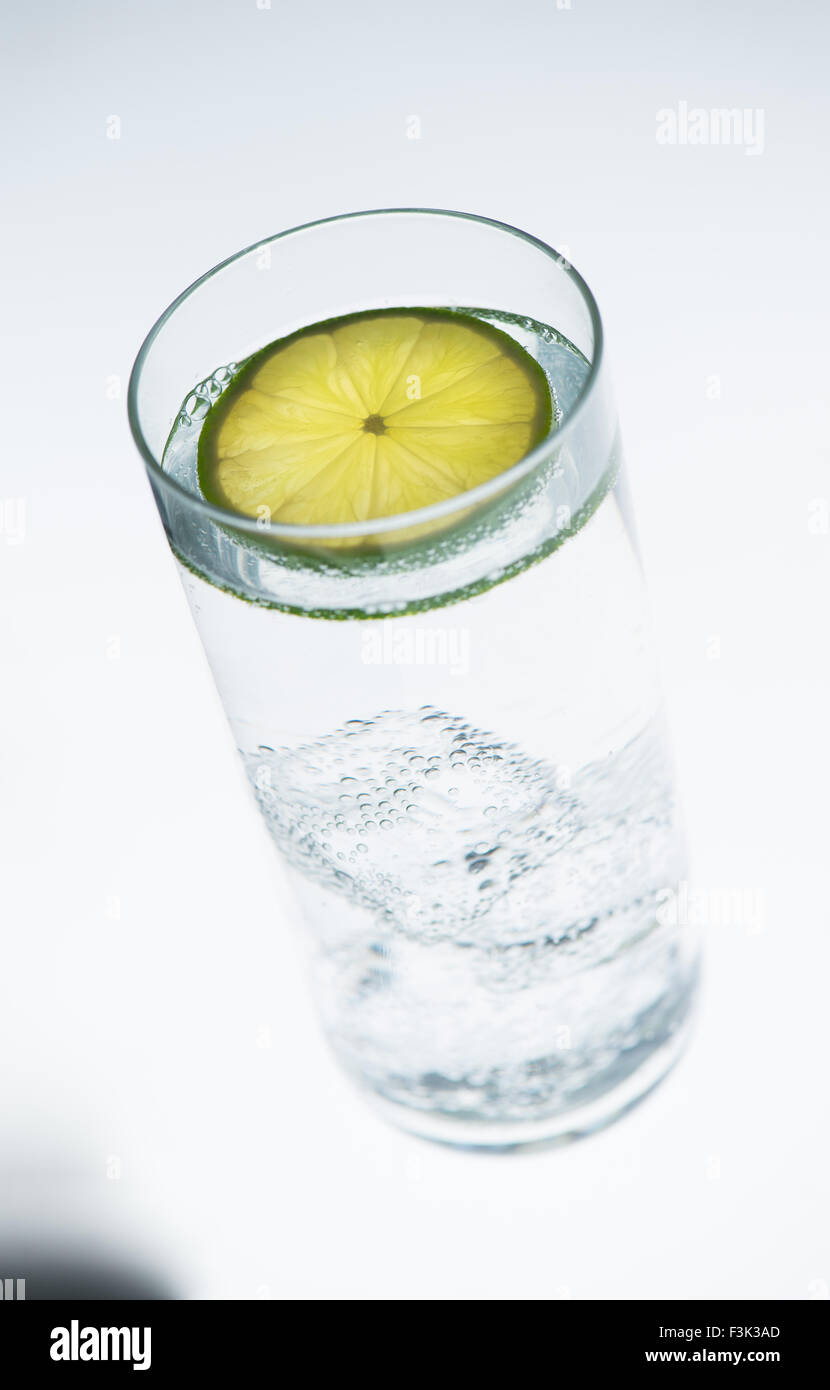 Verre d'eau froide, soda ou boisson alcoolisée avec tranche de lime sur fond blanc Banque D'Images