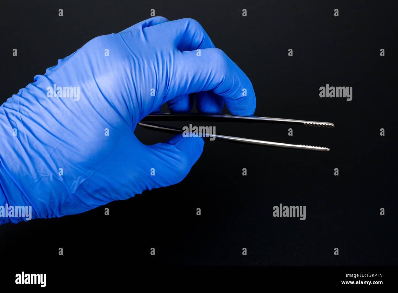 Une main dans un gant médical bleu organise une brucelles à usage médical, affichée sur un tableau noir Banque D'Images