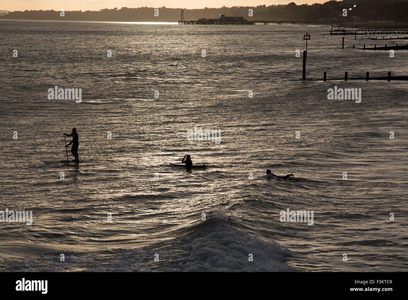 Un homme sur un paddle board et deux surfeurs dans la mer à Bournemouth, Angleterre. Prises en début de soirée la lumière. Banque D'Images