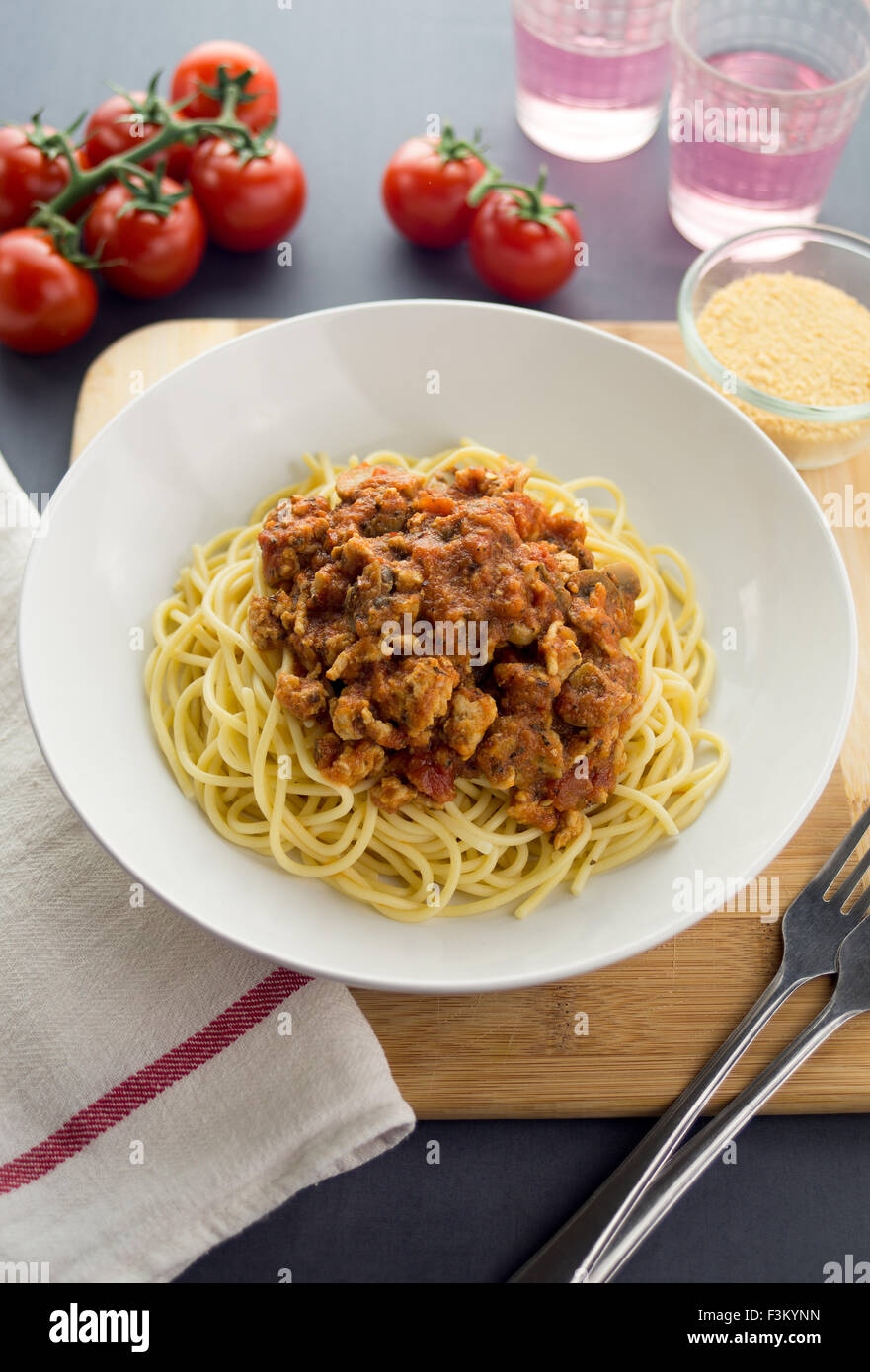 L'Italien spaghetti avec sauce à la viande de poulet et de champignons. Servi dans une assiette blanche avec du parmesan et des boissons. Banque D'Images