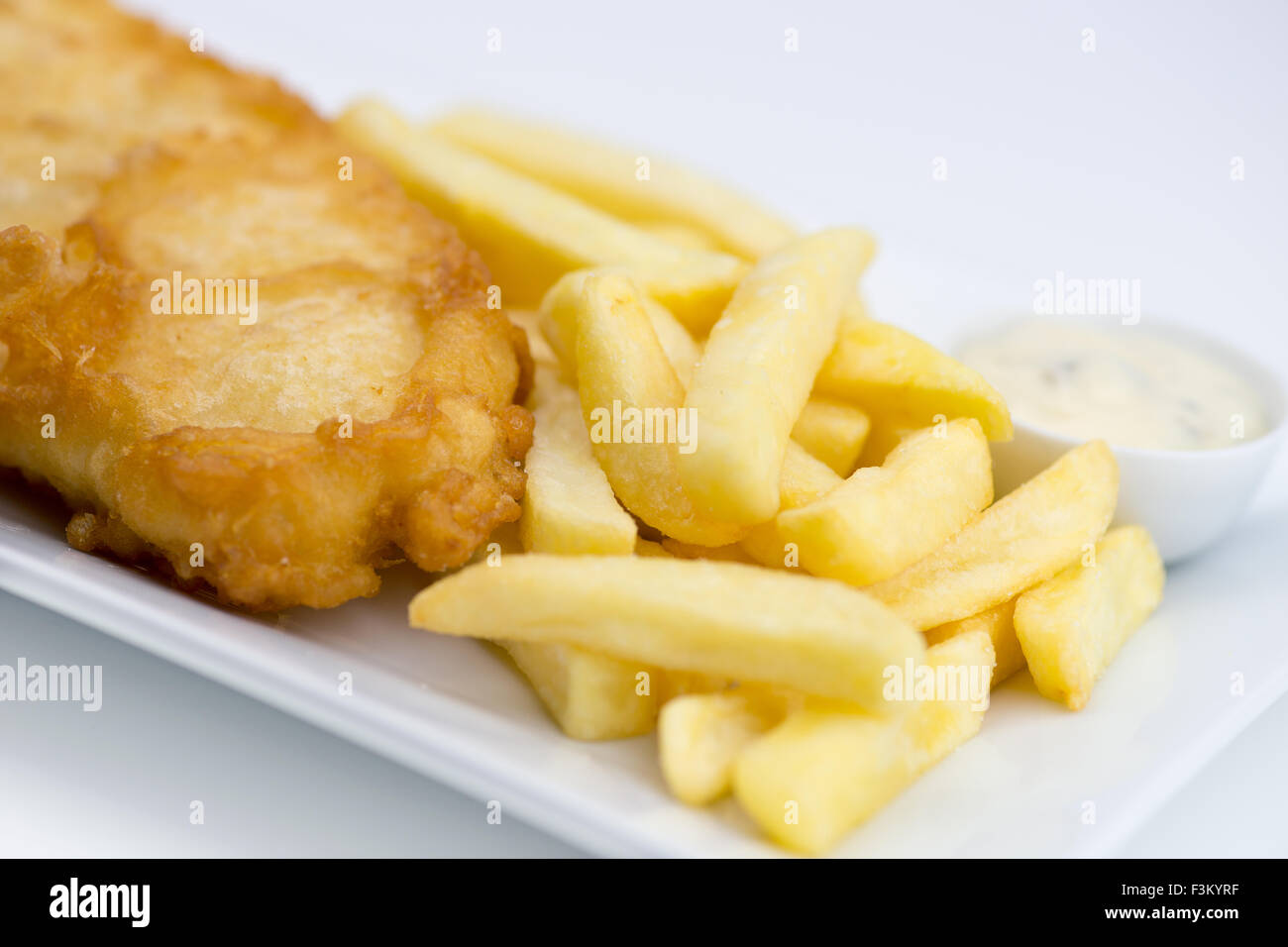 Sauce tartare, frites et poisson pané frit sur une plaque blanche sur un fond blanc. Banque D'Images