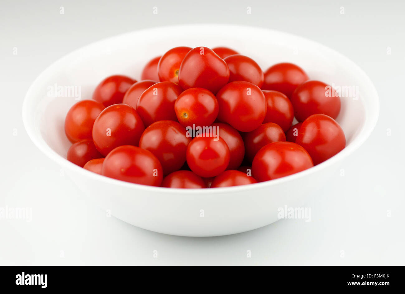 Rouge, tomates cerises juteuses isolé dans une cuvette ronde blanche sur un fond blanc. Banque D'Images