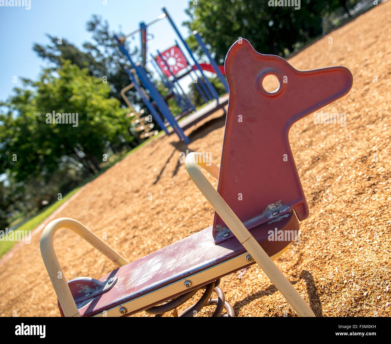 Cheval à bascule rouge en été avec une aire de jeu extérieur et parc à l'arrière-plan Banque D'Images