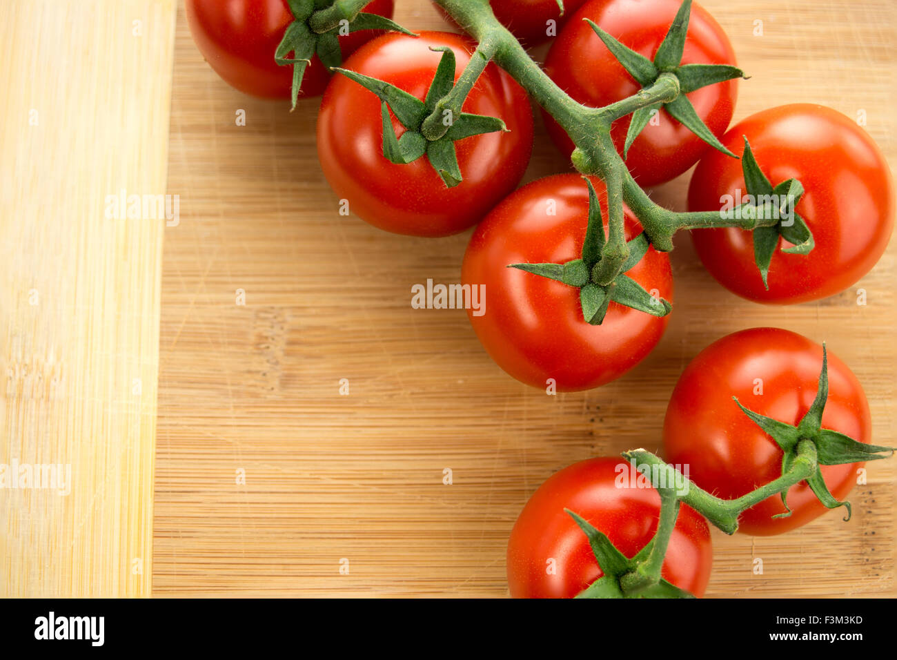 Libre Vue aérienne de tomates cerises avec vignes vertes disposées sur une planche à découper en bois Banque D'Images