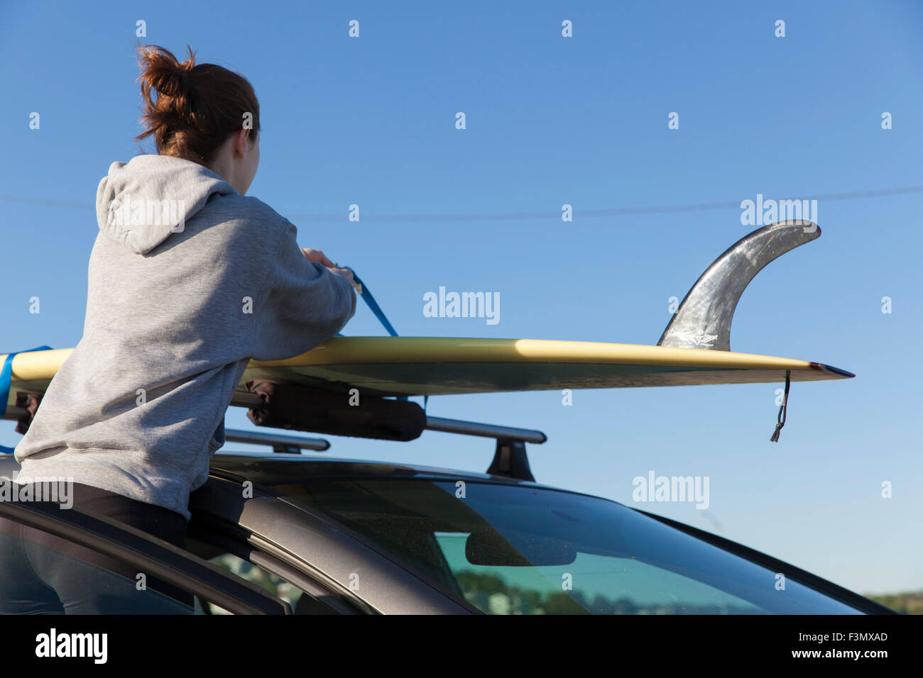 Woman taking surf board off toit de voiture Banque D'Images