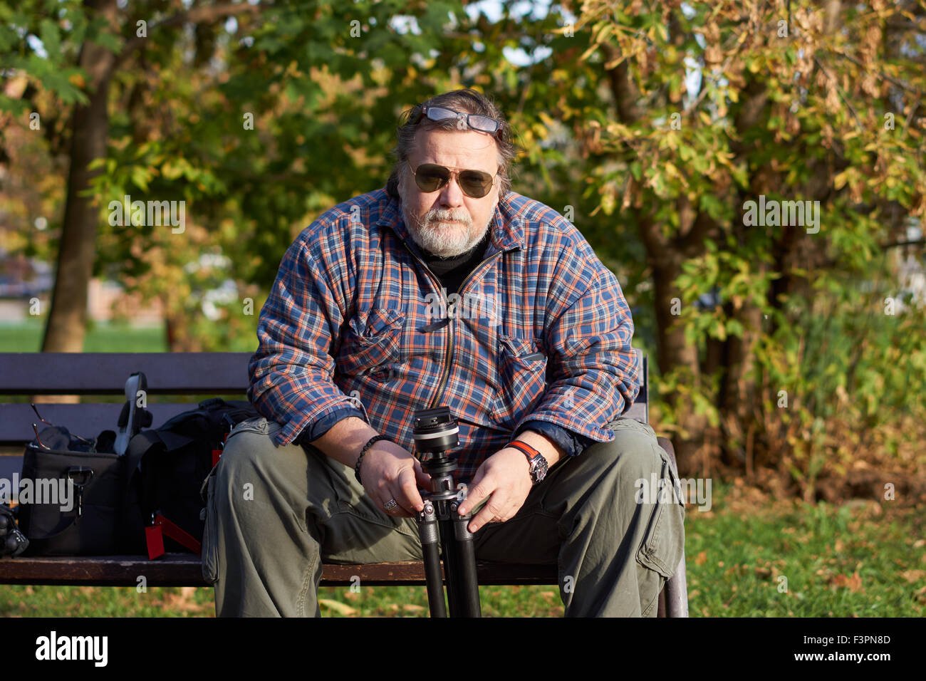 L'homme est assis sur le banc et est titulaire d'un trépied à l'automne Banque D'Images
