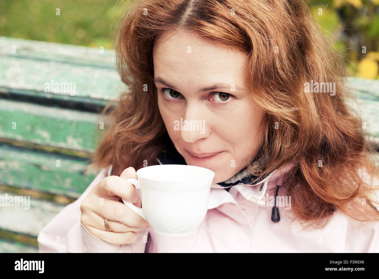 Young adult Caucasian woman boit du café à partir de la tasse blanche dans le parc en automne Banque D'Images