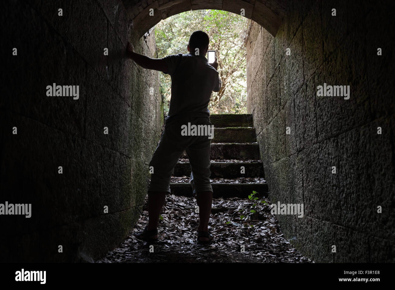 Jeune homme en photo sur son téléphone intelligent à partir de la pierre sombre tunnel Banque D'Images