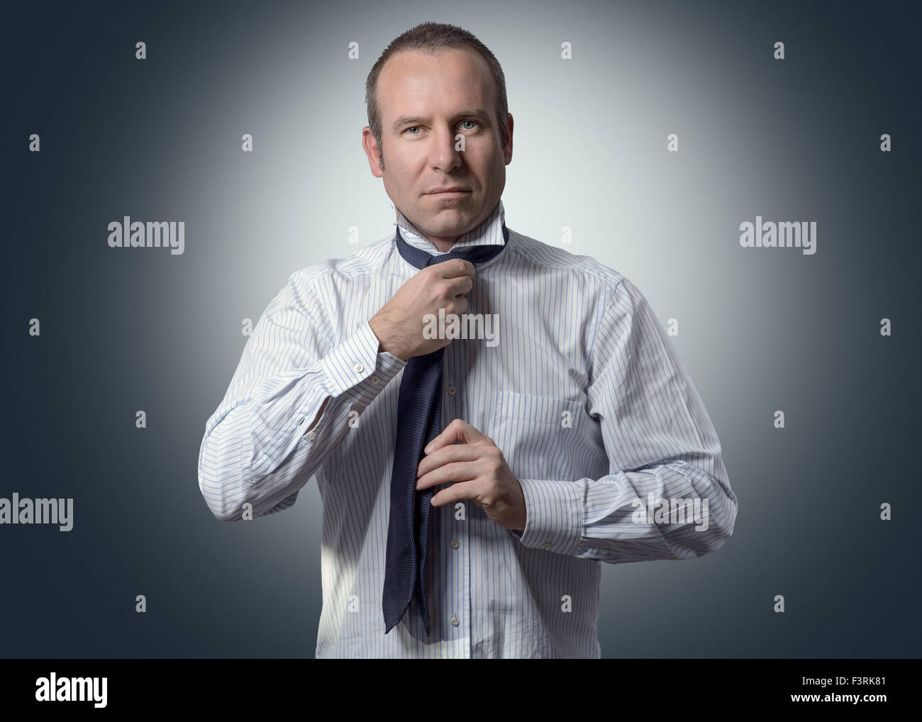 Moitié du corps, tourné d'un adulte Businessman Tying un collier tout en souriant à la caméra contre un arrière-plan gris. Banque D'Images