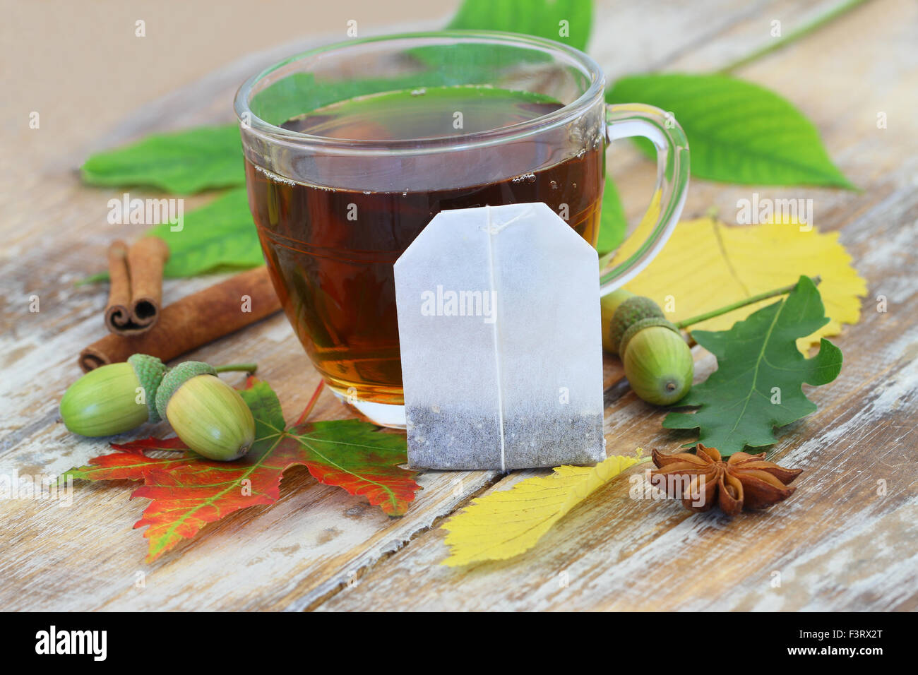 Sachet à thé appuyé contre le verre à thé noir, et les feuilles d'automne Banque D'Images